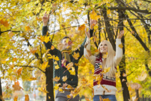 Young couple enjoying falling autumn leaves in park